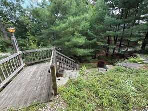 A wooden staircase leading up to a platform with a lamp post, surrounded by dense green foliage and trees. - Ski-in/Ski-out 9 bed log cabin on Pleasant Mountain with Moose Pond lake access (Bridgton)