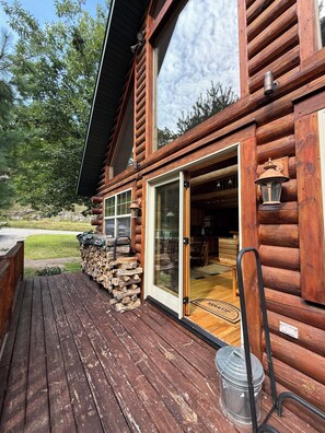 A log cabin with a deck, a sliding glass door, and a visible interior with a dining area. - Ski-in/Ski-out 9 bed log cabin on Pleasant Mountain with Moose Pond lake access (Bridgton)