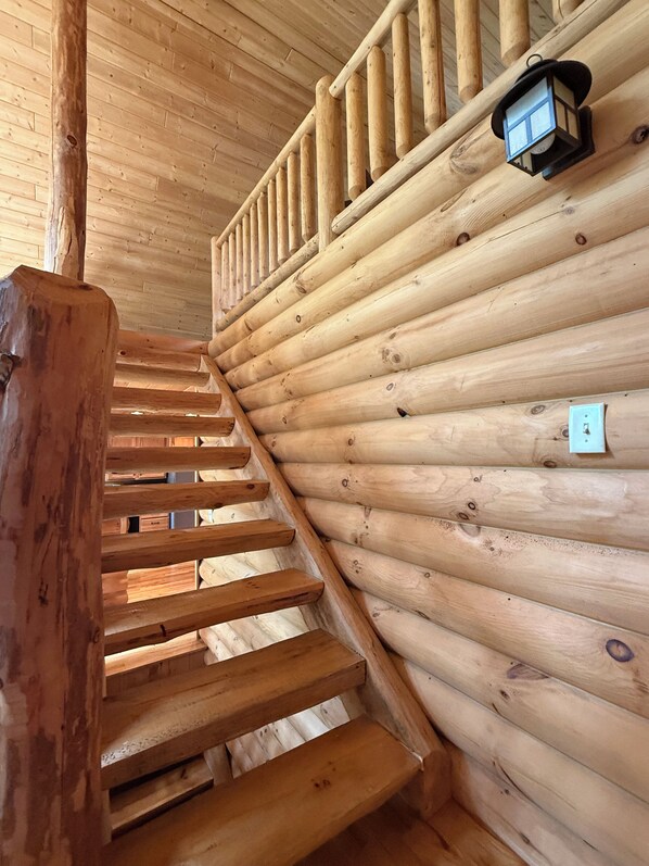A wooden staircase inside a log cabin with a lantern on the wall.