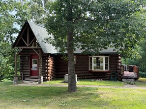 A rustic log cabin with a red door, a chimney, and a small porch.