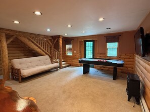 A log cabin interior with a sofa, a pool table, a fireplace, and a television mounted on the wall. - Ski-in/Ski-out 9 bed log cabin on Pleasant Mountain with Moose Pond lake access (Bridgton)
