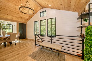 A modern interior with a wooden ceiling, a dining area with a table and chairs, a bench, and a staircase with a railing. - 
Walk to Cashiers - 2 king bed rooms + bunk bed with queen, firepit & secluded (Cashiers)