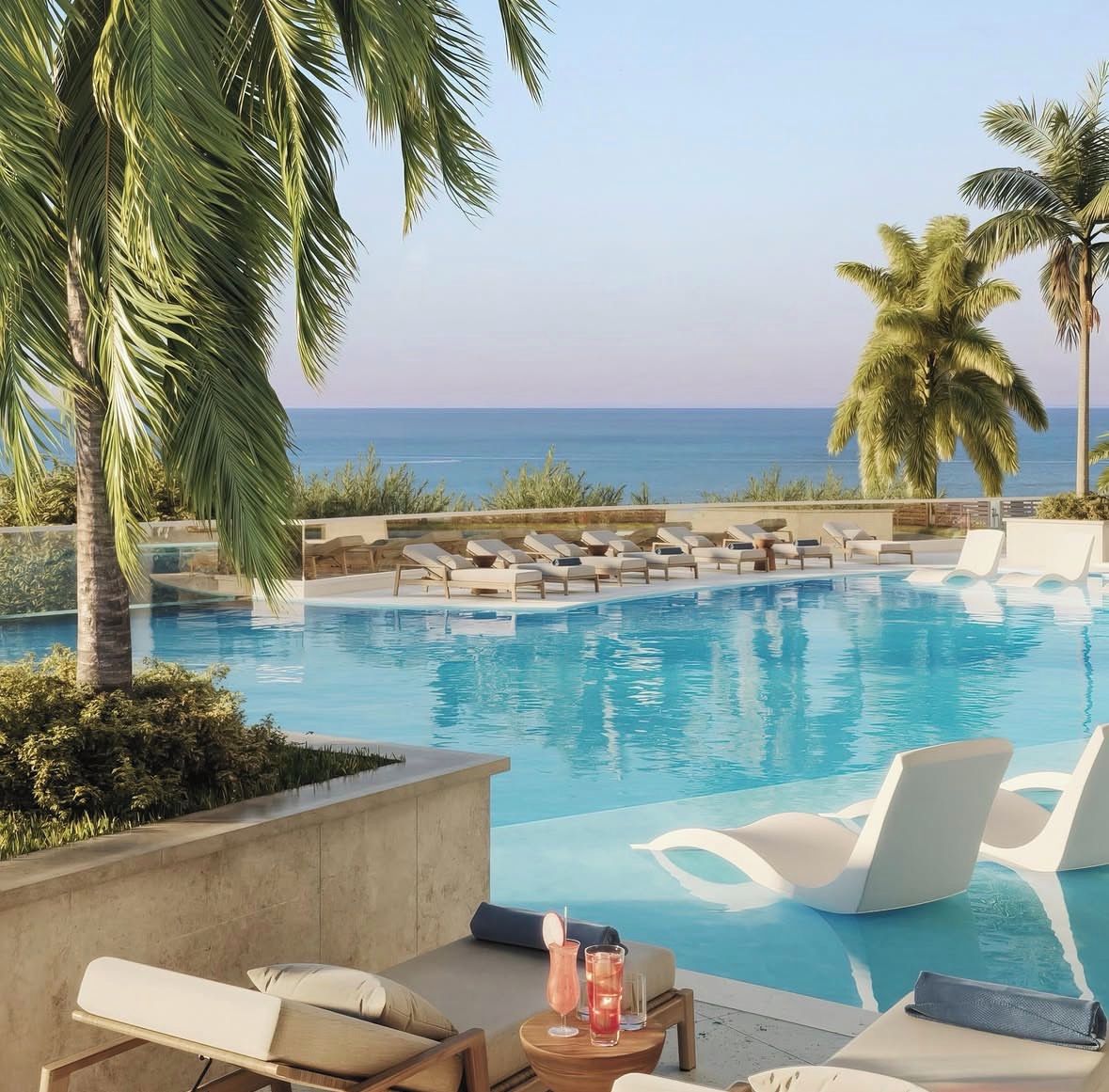 A pool area with lounge chairs and a view of the ocean.