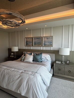 A modern bedroom with a large bed, two bedside tables, a chandelier, and three framed artworks on the wall. - Stunning Ocean Views 4100 sq ft condo in The Ritz-Carlton Residence (Naples)