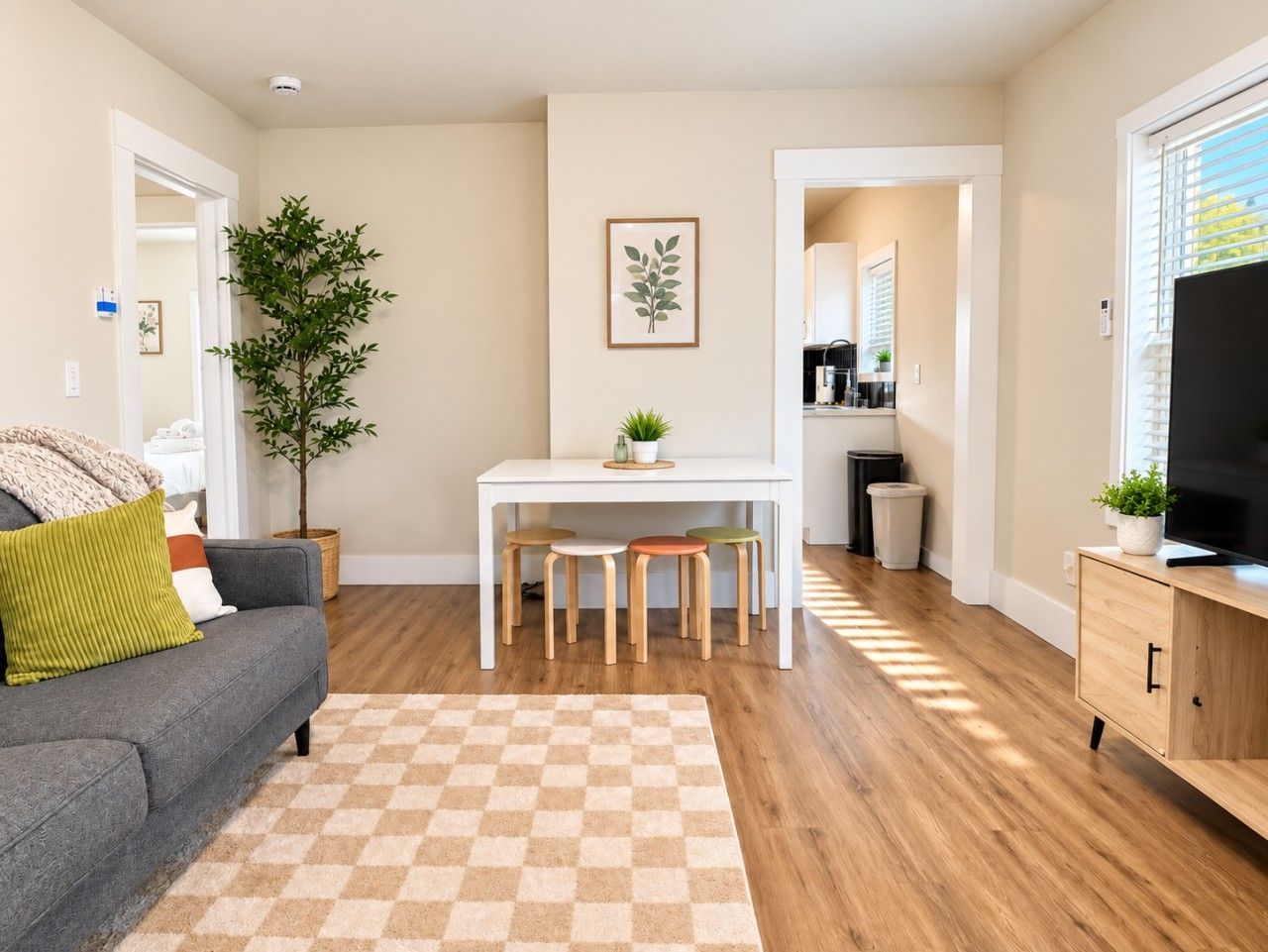 A living room with a sofa, a coffee table, a dining table with stools, a TV, and a kitchen area in the background.