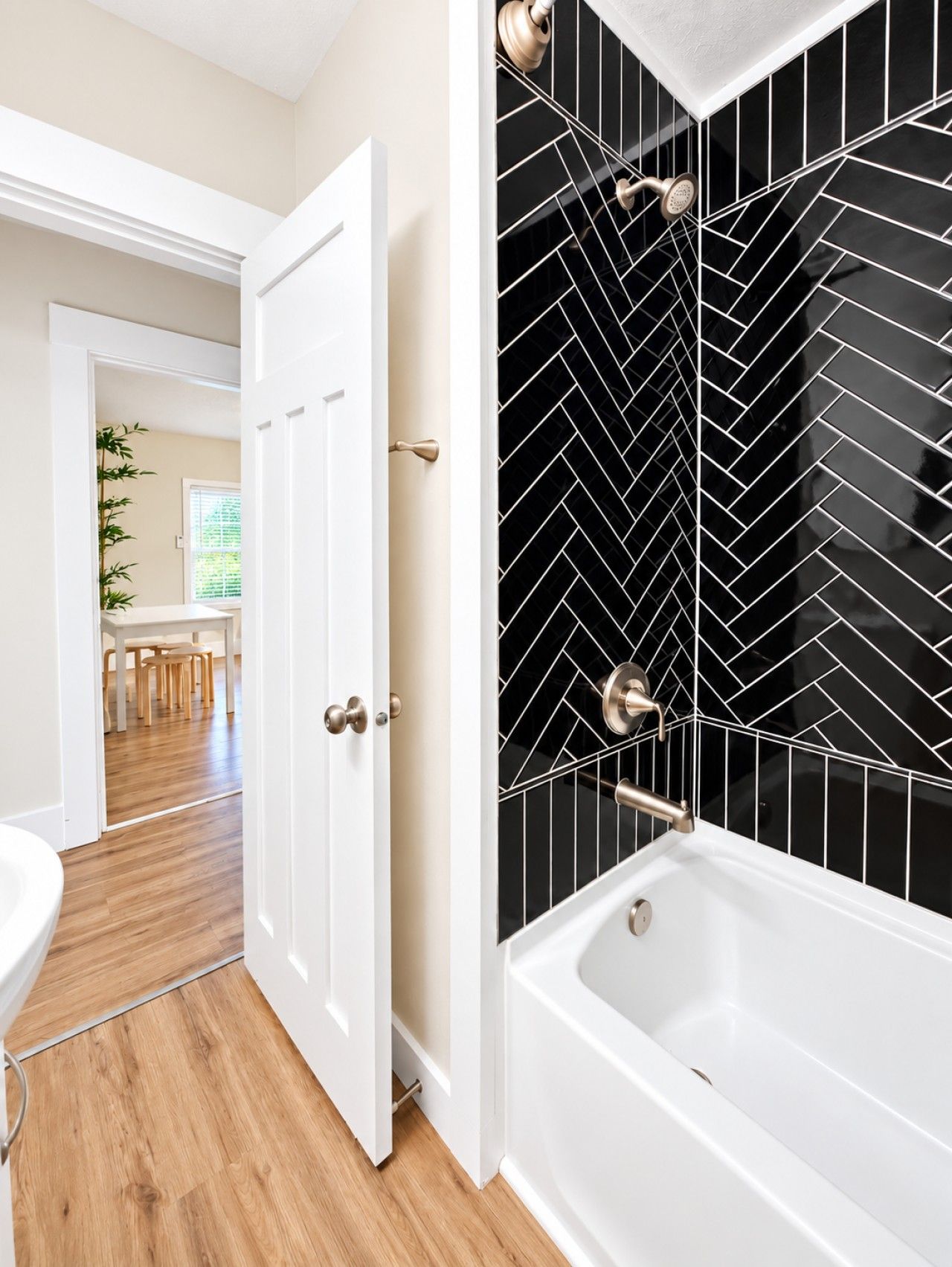A bathroom with a white bathtub, black and white patterned tiles, and a wooden floor.