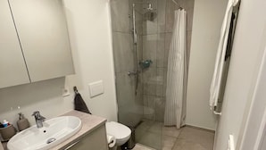 A modern bathroom with a sink, mirror, toilet, shower, and a glass-enclosed shower stall. - Cozy Apartment Near Reykjavík (Hafnarfjordur)
