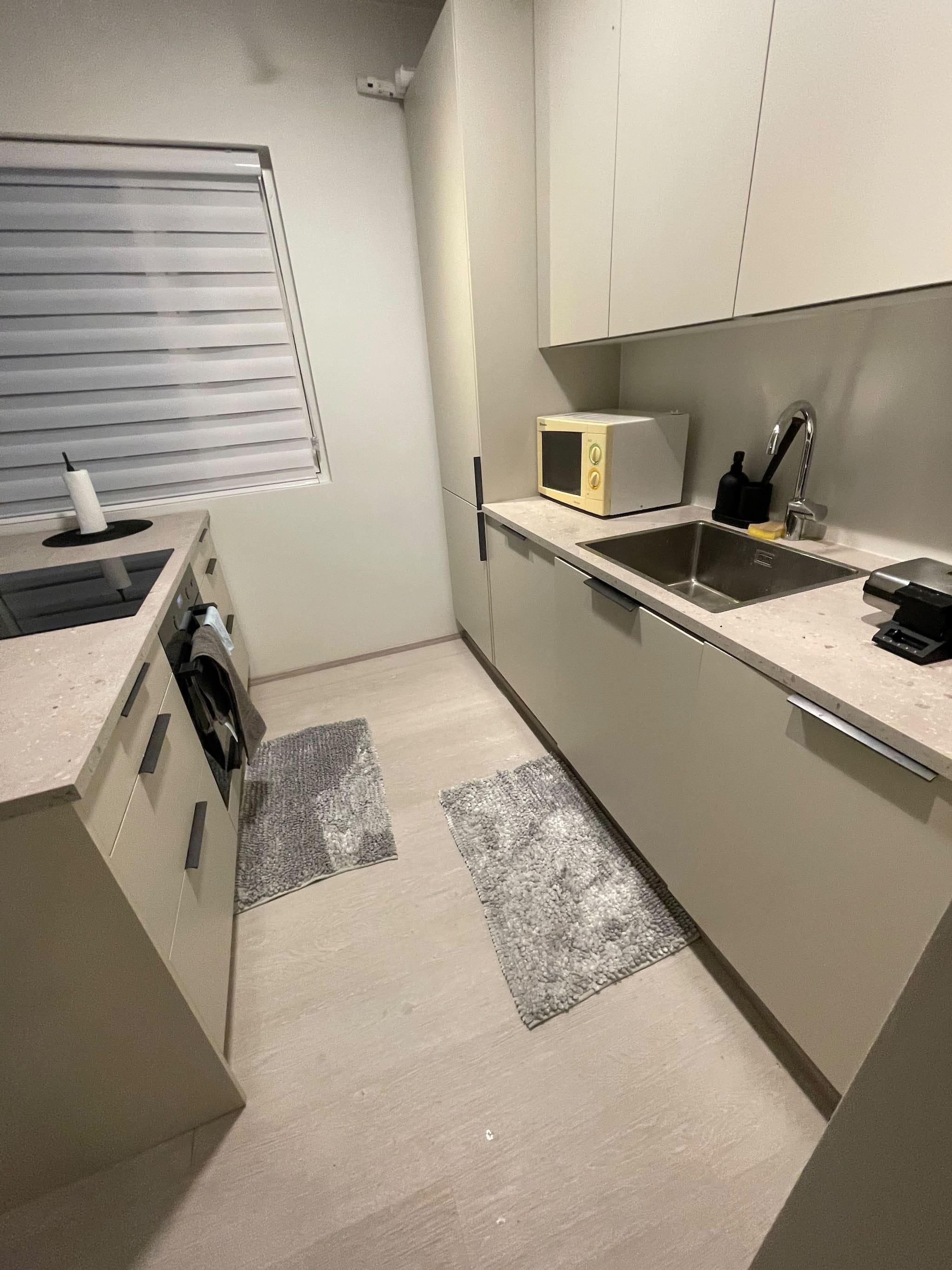 Una cocina compacta con microondas, lavamanos y ventana con persianas.