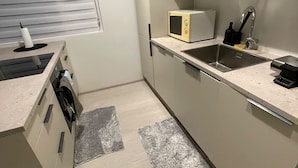 A compact kitchen with a microwave, sink, and a window with blinds. - Cozy Apartment Near Reykjavík (Hafnarfjordur)