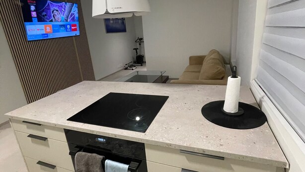 A modern kitchen with a built-in oven, a flat-screen TV mounted on the wall, and a dining area with a sofa. - Cozy Apartment Near Reykjavík (Hafnarfjordur)