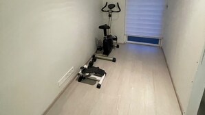 A narrow hallway with a wall-mounted painting, a stationary exercise bike, and a door with a window. - Cozy Apartment Near Reykjavík (Hafnarfjordur)