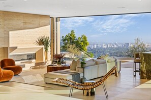 Ein modernes Wohnzimmer mit großem Fenster, einer Couch, einer Hängematte und Blick auf eine Stadtlandschaft.
