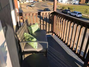 Ein Balkon mit einem Korbssessel und Kissen, mit Blick auf eine Straße mit Autos und Gebäuden.