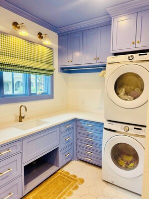 A laundry room with a Samsung washer and dryer, a window with a checkered valance, and a sink with a gold faucet. -  Lovely house within walking distance to TCU (Fort Worth)