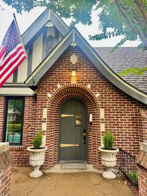 Ein Backsteinhaus mit einer dunkelgrünen Tür, einer US-amerikanischen Flagge und zwei Blumentöpfen.