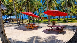 A beach with two picnic tables and red umbrellas, surrounded by palm trees and a clear blue sky. - glampling sanblas luxury (Panamá)