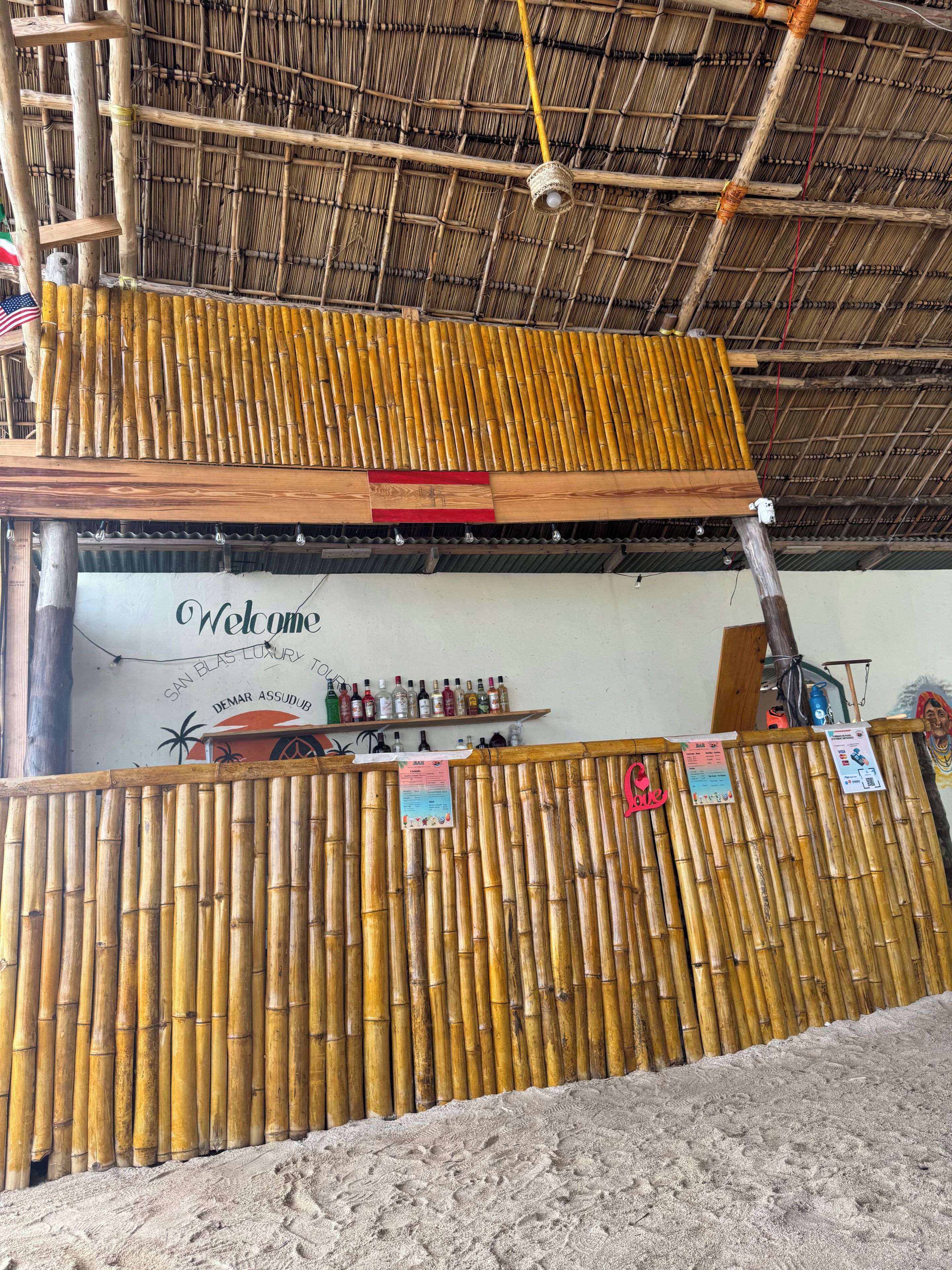A bamboo fence, a welcome sign, and a bar area with bottles.