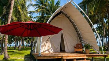 A tent with a wooden deck, a red umbrella, and palm trees in the background.
