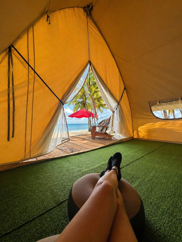 A tent with a view of a beach and palm trees, a red umbrella, and a wooden deck.