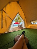 Una carpa con vista a una playa y palmeras, una sombrilla roja y una terraza de madera.