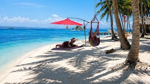 A beach with clear blue water, palm trees, and a red umbrella. - glampling sanblas luxury (Panamá)