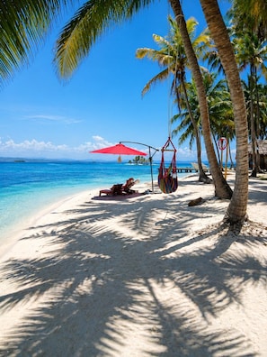Una playa con agua azul cristalina, palmeras y un paraguas rojo.