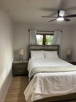 A bedroom with a bed, two bedside tables with lamps, a ceiling fan, a window with curtains, and a view of greenery outside. - Marvelous 3-bedroom house with a private pool in Albuquerque. (Albuquerque)