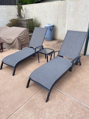Two lounge chairs with armrests and a small table, positioned on a patio with a concrete floor and a covered table to the left. - Marvelous 3-bedroom house with a private pool in Albuquerque. (Albuquerque)