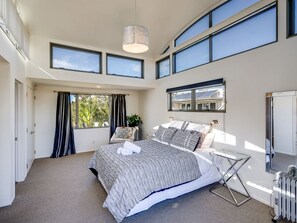 A modern bedroom with a large bed, multiple windows, and a ceiling light. - Napier Sea Views | Hawke's Bay (Napier)