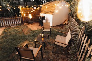 Un patio trasero con una terraza de madera, una parrilla y luces colgantes.