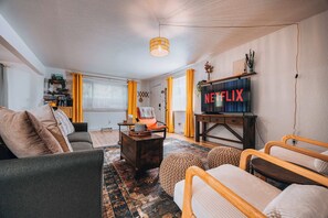 Ein Wohnzimmer mit einer Couch, Sesseln, einem Couchtisch, einem Fernseher und einem Kamin.
