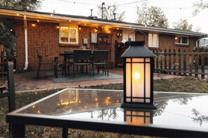 Un área de patio al aire libre con una mesa de vidrio, sillas de mimbre y un farol.