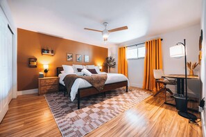 Ein modernes Schlafzimmer mit einem Bett, Nachttischen, einem Deckenventilator und einem Fenster mit Vorhängen.