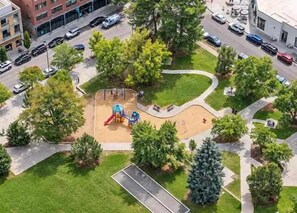 Vista aérea de un parque con un área de juegos, rodeado de árboles y un estacionamiento.