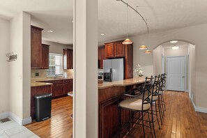 A kitchen with wooden cabinets, a stainless steel refrigerator, a bar area with stools, and pendant lighting. - Great Location! Fireplace! Luxury Bathrooms! (Branson)