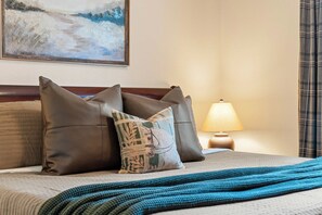 A hotel room with a bed, pillows, a blanket, a painting on the wall, and a lamp. - Great Location! Fireplace! Luxury Bathrooms! (Branson)