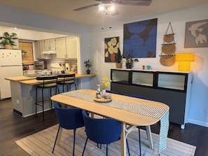 Une cuisine moderne avec un coin repas, comprenant une table en bois, des chaises bleues et un ventilateur de plafond.