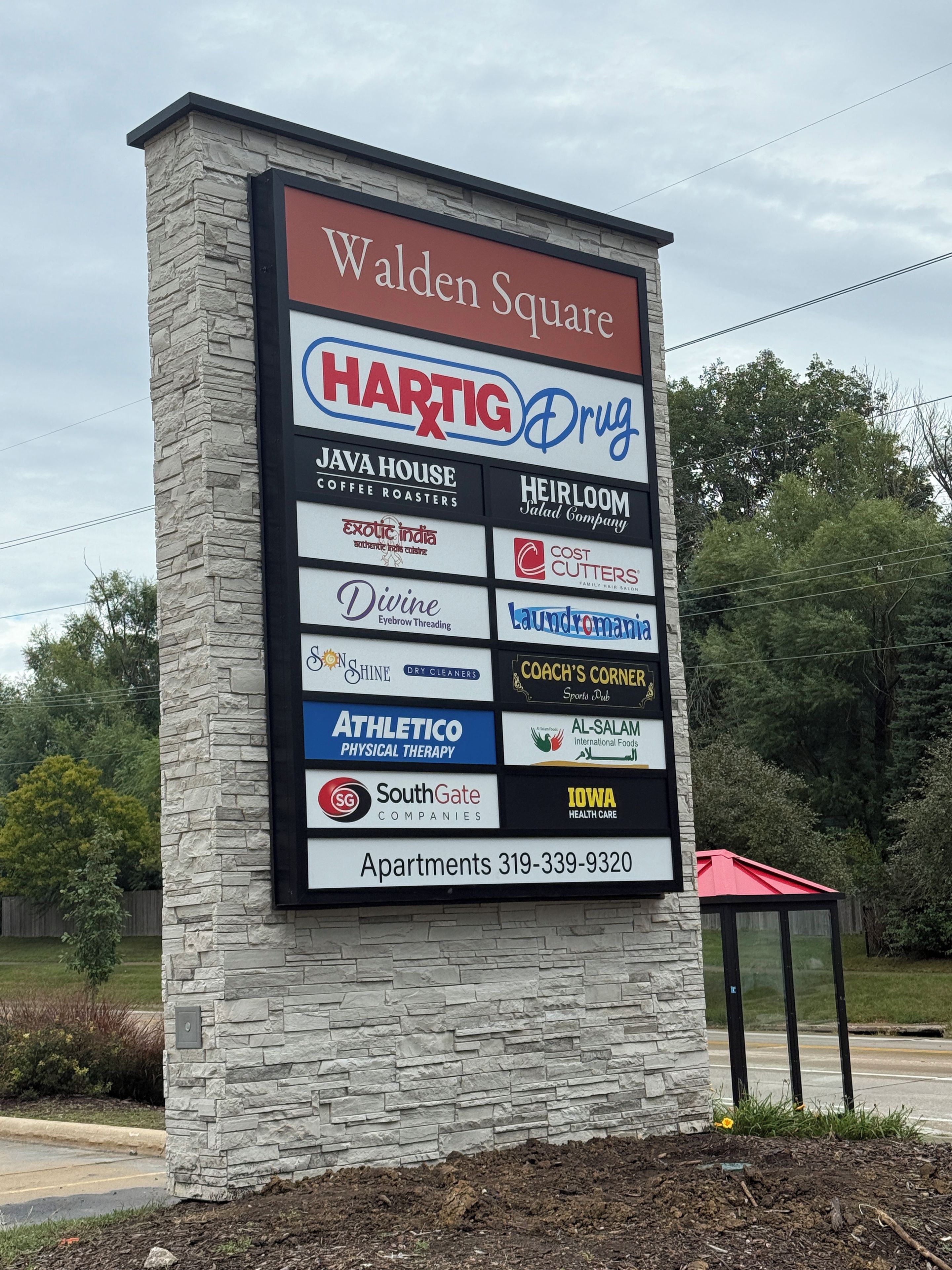 A commercial signboard with multiple business names and a contact number for apartments.