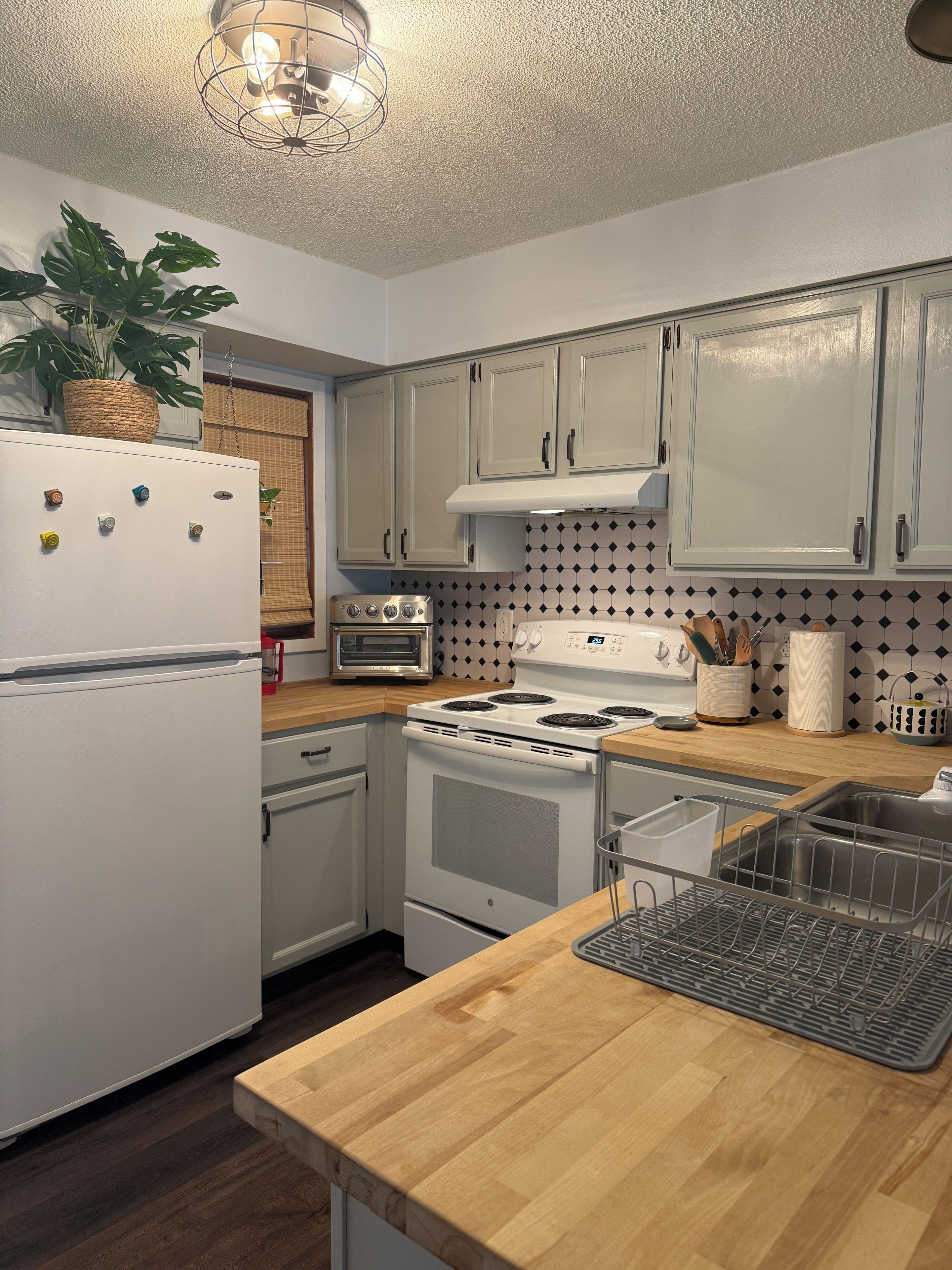 A kitchen with white cabinets, a stove, an oven, a refrigerator, and a wooden countertop.