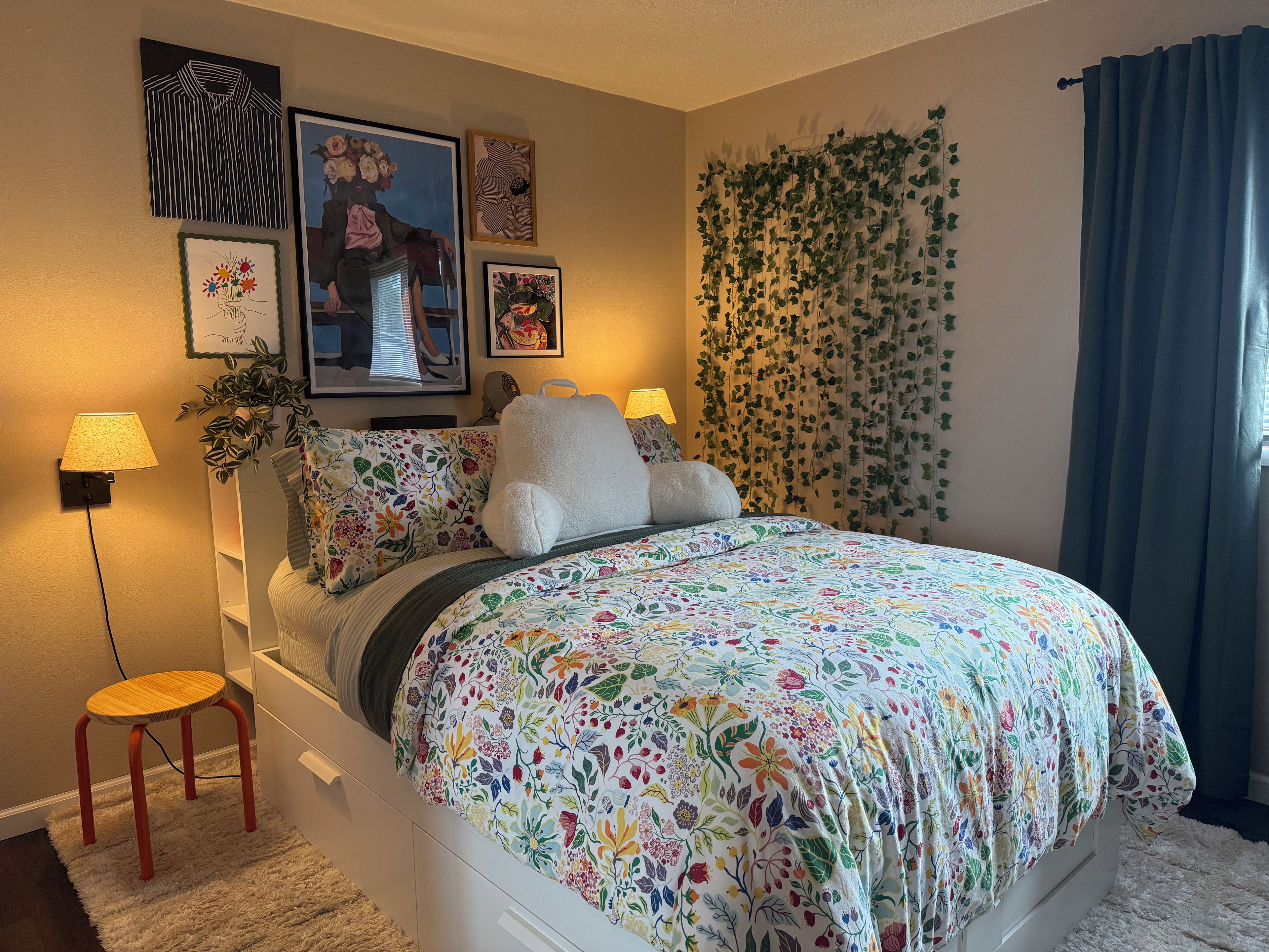 A bedroom with a bed, a nightstand, a lamp, a chair, and a wall with framed artwork.