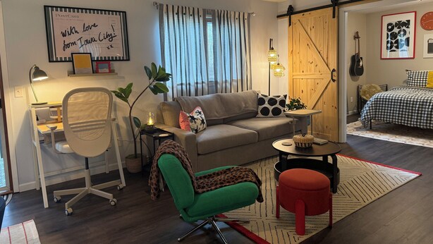 A modern living room with a sofa, a desk, a chair, and a dining area with a table and chairs.