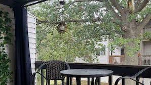 A covered porch with a table and chairs, a patterned rug, and a view of a tree and house.