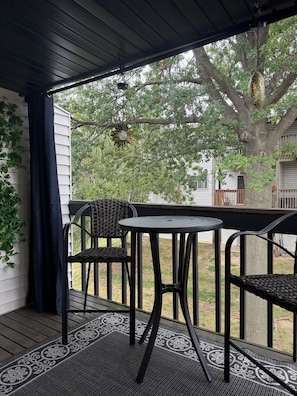 Une véranda abritée avec une table et des chaises, un tapis à motifs et une vue sur un arbre et une maison.