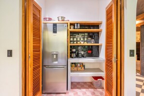 A compact kitchen with a built-in refrigerator, a coffee maker, and shelves with jars and kitchen utensils. - Casa Tapa Dulce | Spacious Jungle Home with Pool (Paraíso)