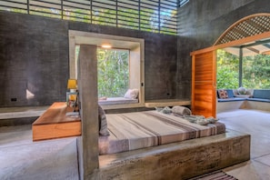 A modern room with a bed, a wooden bench, a reading area, and a view of greenery. - Casa Tapa Dulce | Spacious Jungle Home with Pool (Paraíso)