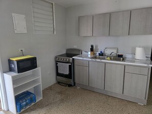 Eine kompakte Küche mit Herd, Backofen, Spüle und einer Mikrowelle auf einem Regal.
