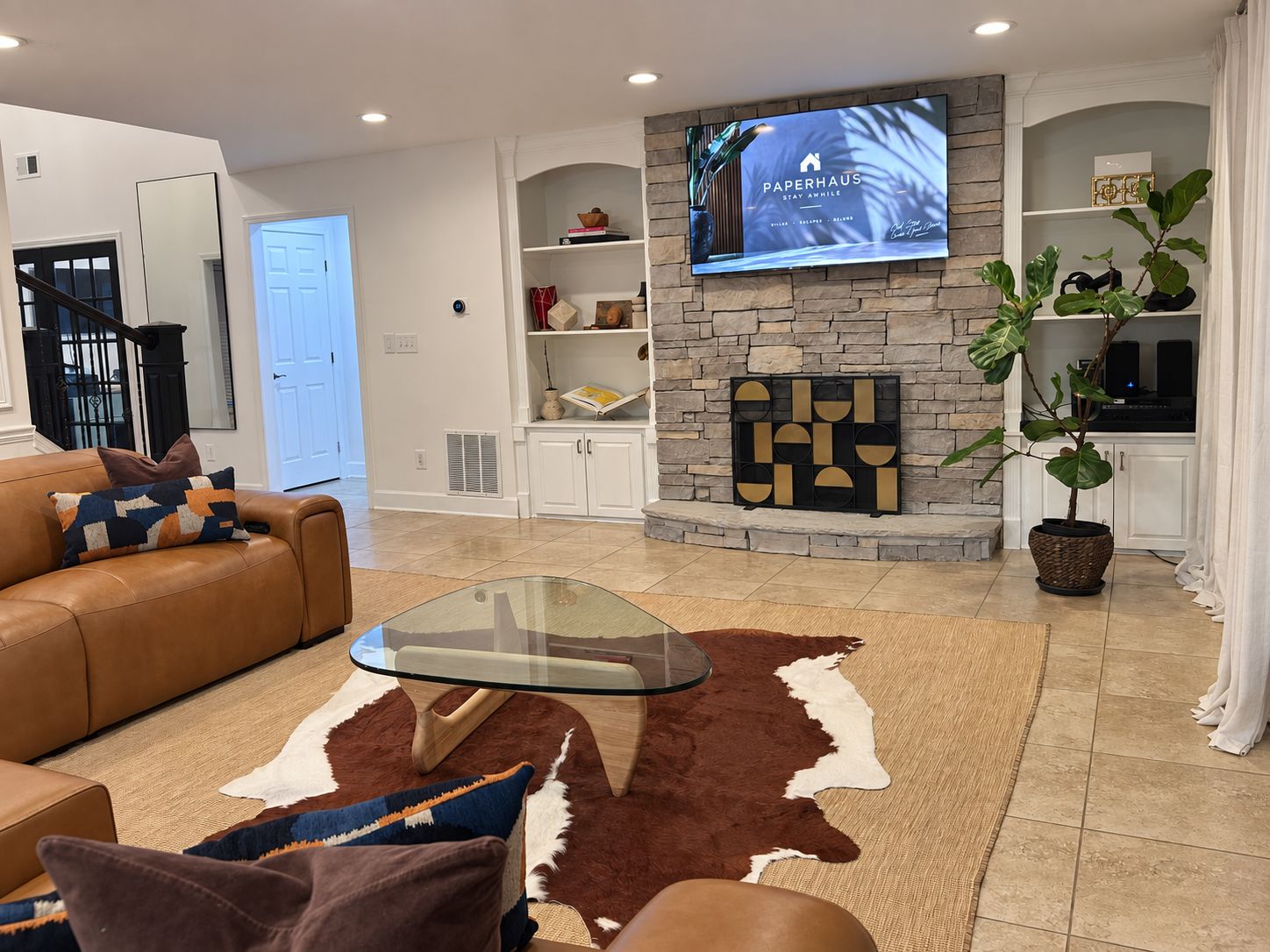 Una sala de estar moderna con chimenea de piedra, un televisor de pantalla plana montado encima y una mesa de centro de cristal, además de un sofá de cuero.