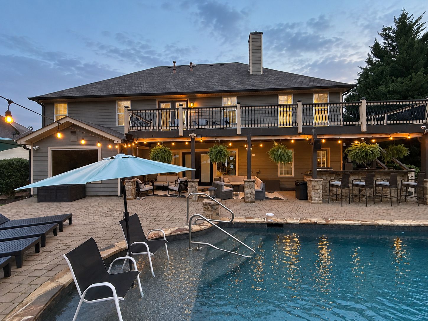 A two-story house with a swimming pool, outdoor seating, and string lights.