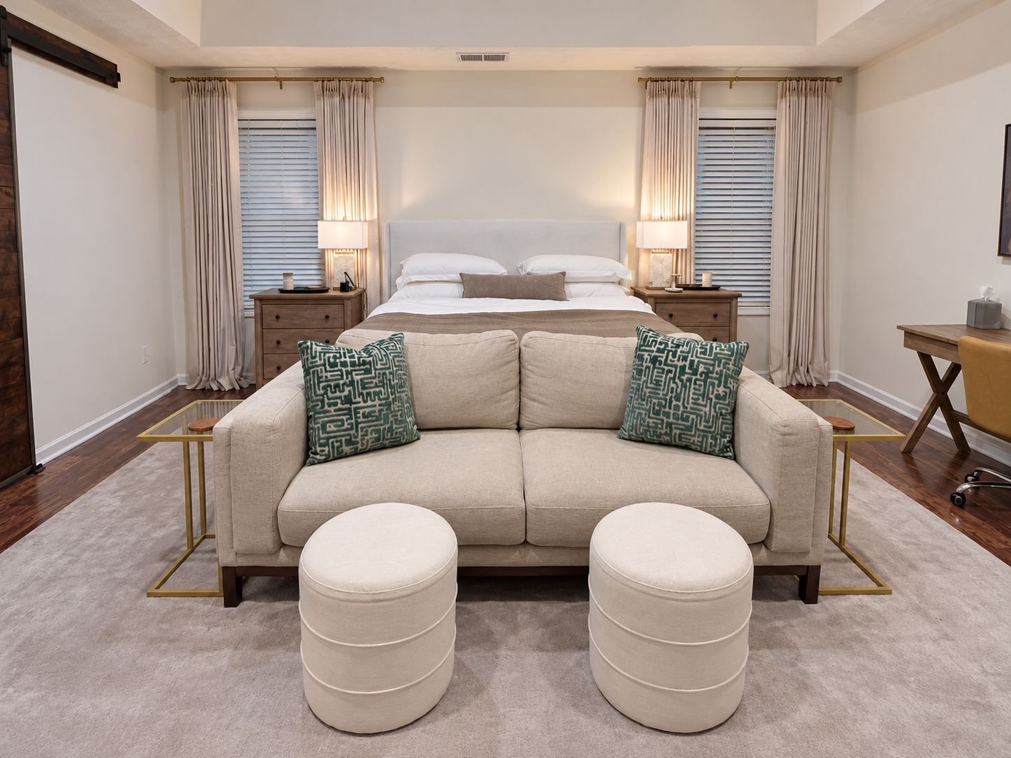 A bedroom with a bed, bedside tables, a sofa, ottomans, and a desk.