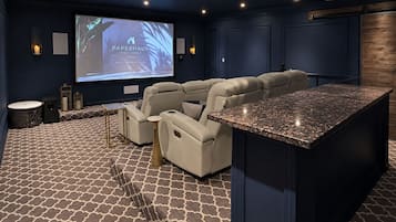 A home theater with a large screen, plush seating, and a small bar area.